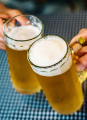 Close-up view of a two glass of beer in hand. Beer glasses clinking at bar or pub