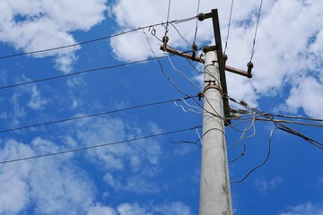 An electric pole with multiple wires under cloudy blue sky