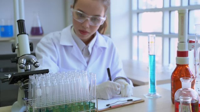 Young female scientists took a test tube to analyze and use a pen to record the results on paper.