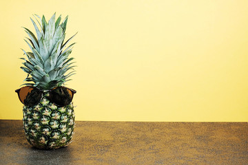 Cool ananas with sunglasses on yellow background