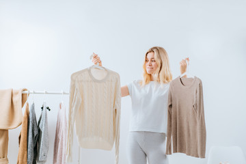 Young pretty girl blogger stands with a thoughtful expression on his face on the background of clothes hanging on a hanger in the wardrobe