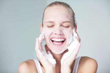 Woman cleaning her skin and washing her face whilst laughing. Foaming facial.