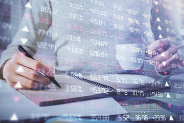 Forex chart hologram on hand taking notes background. Concept of analysis. Double exposure