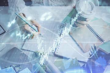 Financial forex graph displayed on hands taking notes background. Concept of research. Multi exposure