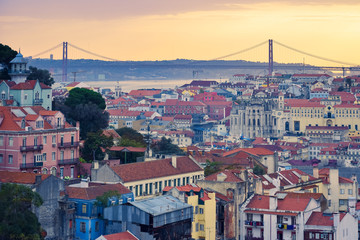 Fototapeta na wymiar Lisbon panoramic view. Colorful walls of the buildings of Lisbon, with orange roofs and the 25th of April bridge in the background, at sunset. Travel and real estate concept. Lisbon, Portugal. Europe
