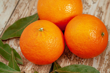 Three ripe tangerines on a wooden background next to green leaves close-up with selective focus.