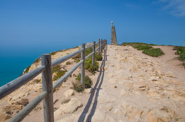Portugal, Cabo da Roca, The Western Cape Roca of Europe, hiking trails on the Cape Roca,  wooden handrails at the  stone road,  a cross on the top of the monument at Cabo da Roca