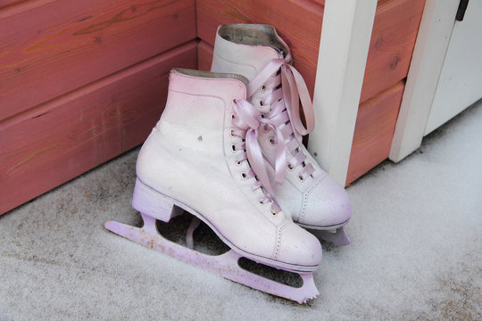 a pair of vintage white skates with pink ribbons standing outside in the snow