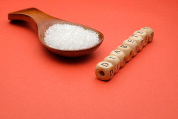 Health concept. Sugar in a wooden spoon with a DIABETES wording on red background