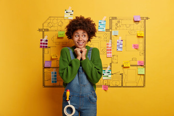Indoor shot of happy woman develops project on new recently bought apartment, keeps hands under...