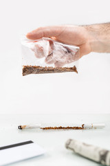 The concept of nicotine dependence and tobacco Smoking. A man's hand holds a bag of tobacco, and at the bottom is a dollar bill, a Bank card, and a broken cigarette. White background. Copy space
