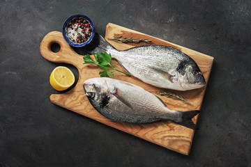 Fresh raw dorado fish on a wooden cutting board, dark rustic background. View from above