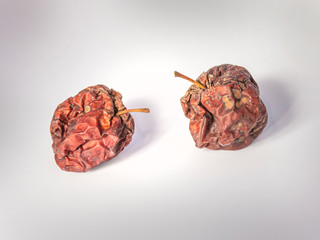 Two dried whole apples on a shiny background. Wrinkled, blackened and ugly. Symbols of old age. - 312759328
