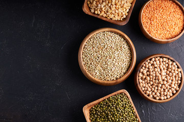 Assortment of cereals, legumes, cereals, grains, lentils, chickpeas, peas, beans, oatmeal in wooden bowls on a dark background