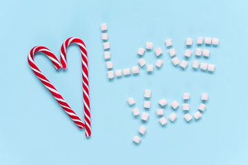 The heart of two Christmas red-white candy sticks on a bright blue background. Love you, Valentine's Day, Christmas, Winter, New year
