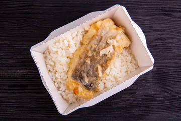 Fried fish with boiled rice in disposable dishes