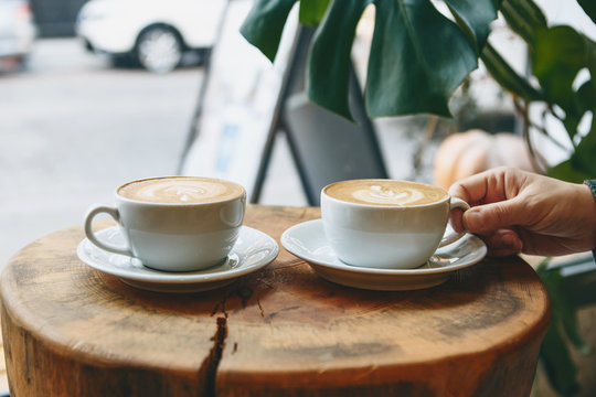 Two cups of aromatic coffee cappuccino or latte on a wooden table. person holds a cup with hand. Concept of meeting or relaxing. Tasty morning drinks.
