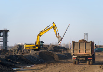 Excavator load the sand to the dump truck on construction site. Backhoe digs the ground for the foundation and construction of a new building.