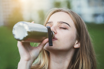 portrait of pretty young blonde woman drinking water from stainless steel bottle