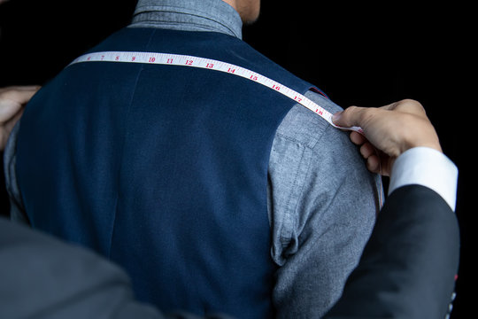 The dressmaker was measuring the width of the back of the man wearing a blue suit on black background.