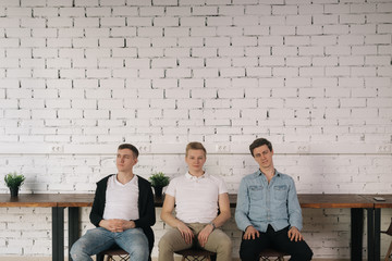 Three young adult man candidates are sitting in the hallway waiting for a job interview. Recruiting and employment concept.