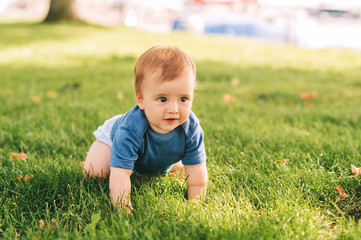 Adorable red haired baby boy crawling on fresh green grass in summer park