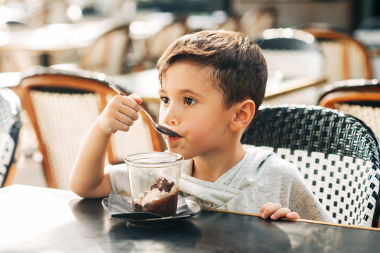 Happy little boy eating chocolate ice cream in outdoor cafe