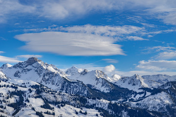 snowy swiss alps mountains in the sun in a blue sky with ufo shaped clouds