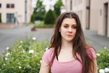 street portrait of a serious young woman with long brunette hair outdoor. Beautiful young female in...
