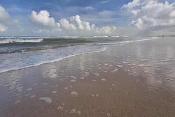 Fototapeta na wymiar Fale na brzegu morza, niebieskie niebo i białe chmury w słoneczny letni dzień.