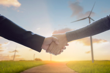 Businessperson handshake working with modern virtual technology with wind turbines in background as concept of renewable business and environmental conservation.