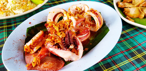 Close up fried octopus or squid with garlic stir on banana leaf in blue dish or plate for lunch at Thai local food restaurant