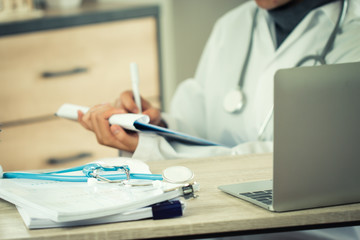 Healthcare and medical concept, Asian Doctor Female physician writing prescription clipboard in uniform, working laptop computer, stethoscope document in hospital. health care information of patient