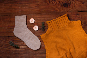 Cozy flatlay. Knitted socks, orange sweater, candles, fir branches on wooden background flat lay.Winter holidays concept.Warm weekend cold weather. Trendy knitted clothes, top view. Fashion design.