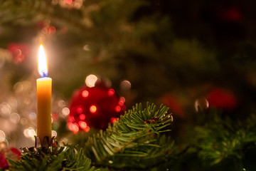single candle on a decorated christmas tree and bokeh