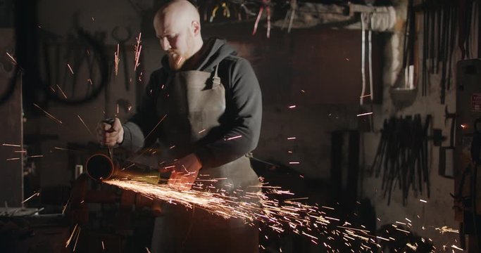 Young blacksmith with angle grinder sparks in his workshop dark and eerie