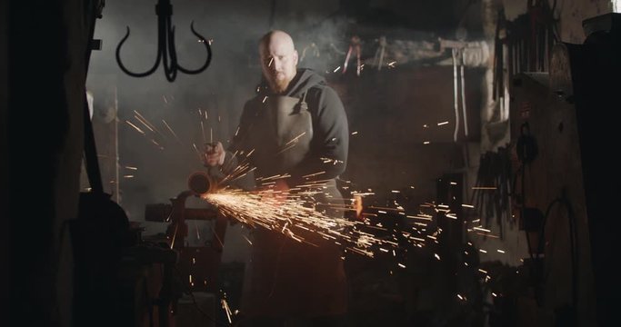 Young blacksmith with angle grinder sparks in his workshop dark eerie haze