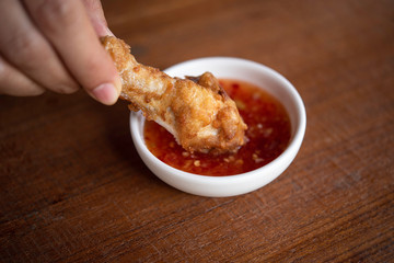 Deep-fried chicken wings are dipped in chili sauce.