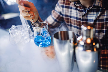 Barman mixes blue cocktail show with colorful alcoholic and smoke bar counter