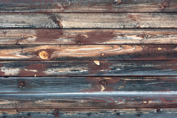 Fragment of the wall of an old wooden building. Boards are located horizontally. Wood sheathing, faded and blackened. There are residues of brown paint. Background. Texture.