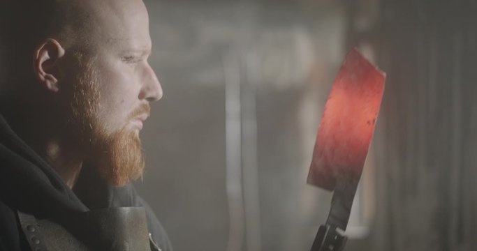 Portrait of young blacksmith looking at knife dark eerie haze