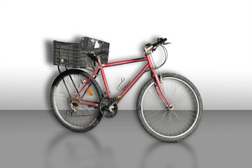 Red old rusty bicycle with tatty gray plastic box on carrier, casting shadow on neutral background