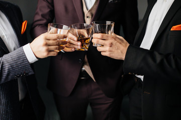 Close-up partial view of three friends clink glasses of whiskey drink, alcoholic beverage. Men in...
