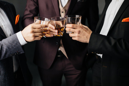 Close-up Partial View Of Three Friends Clink Glasses Of Whiskey Drink, Alcoholic Beverage. Men In Formal Wear Toasting With Glasses Of Whiskey. Whisky Drink