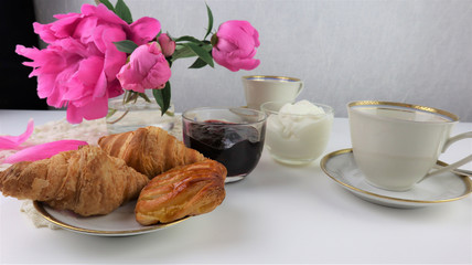 breakfast with two cups of coffee and croissants, bouquet of pink flowers peonies