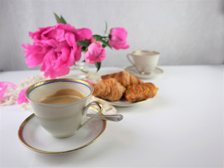 breakfast with two cups of coffee and croissants, bouquet of pink flowers peonies