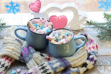 A pair of cups with a drink decorated with meringues and marshmallows, Christmas decor, hearts, knitted scarf on the windowsill, home comfort concept, winter holidays