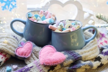 Obraz na płótnie Canvas A pair of cups with a drink decorated with meringues and marshmallows, Christmas decor, hearts, knitted scarf on the windowsill, home comfort concept, winter holidays