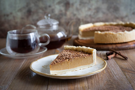 A piece of pumpkin pie with chocolate on a stylish white plate close up on a wooden table