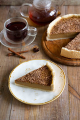 A piece of pumpkin tart with chocolate chips, a Cup of hot tea, and a pumpkin pie on a wooden table. Vertical photography